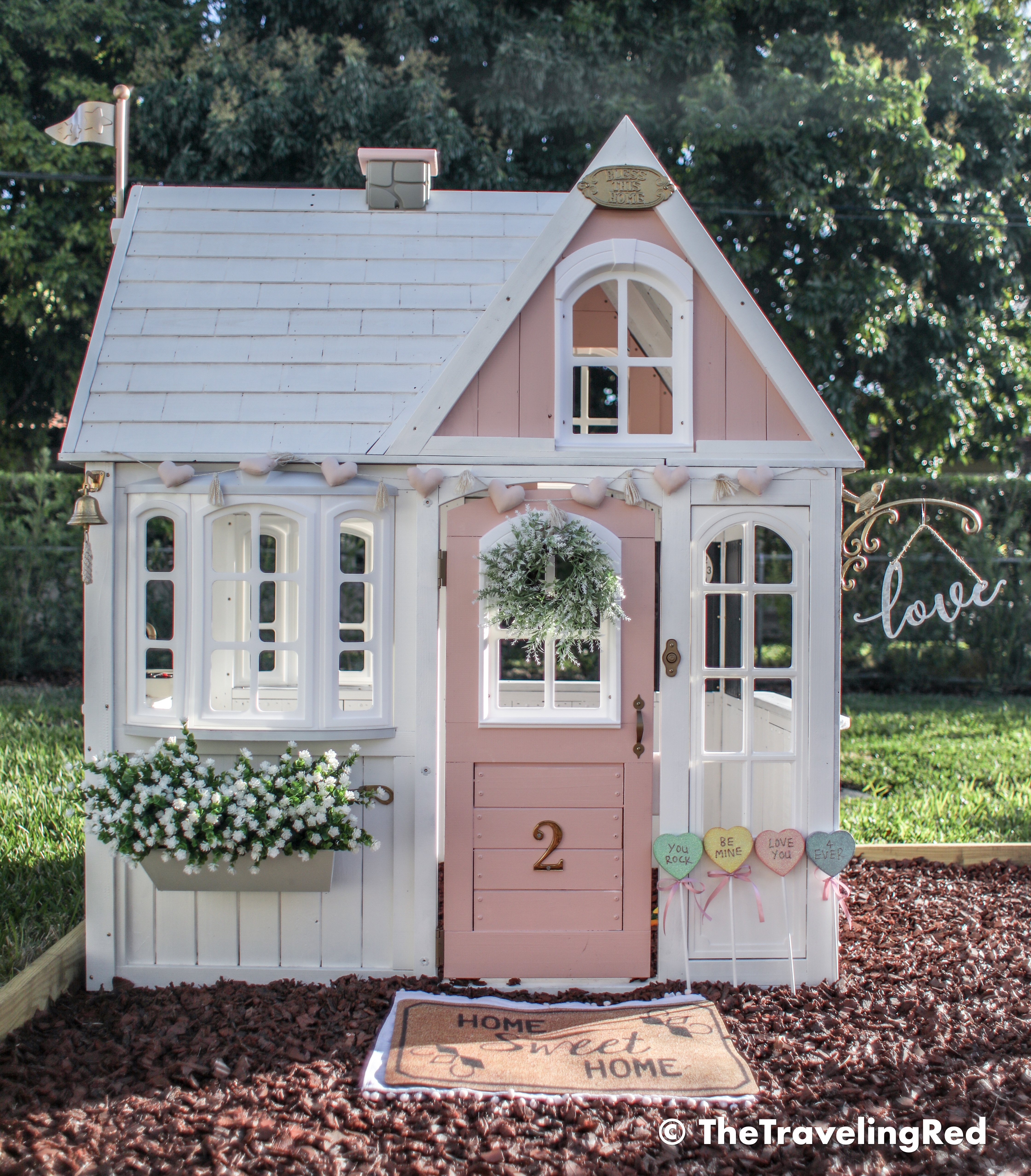 Valentine's Day Playhouse Decor - Kid's outdoor playhouse makeover decorated for Valentines Day using garland, candies and a little sign. Pink & white outdoor playhouse #valentinesday #valentinesdaydecor #homedecor #playhouse #playhousemakeover #valentinesdayhomedecor