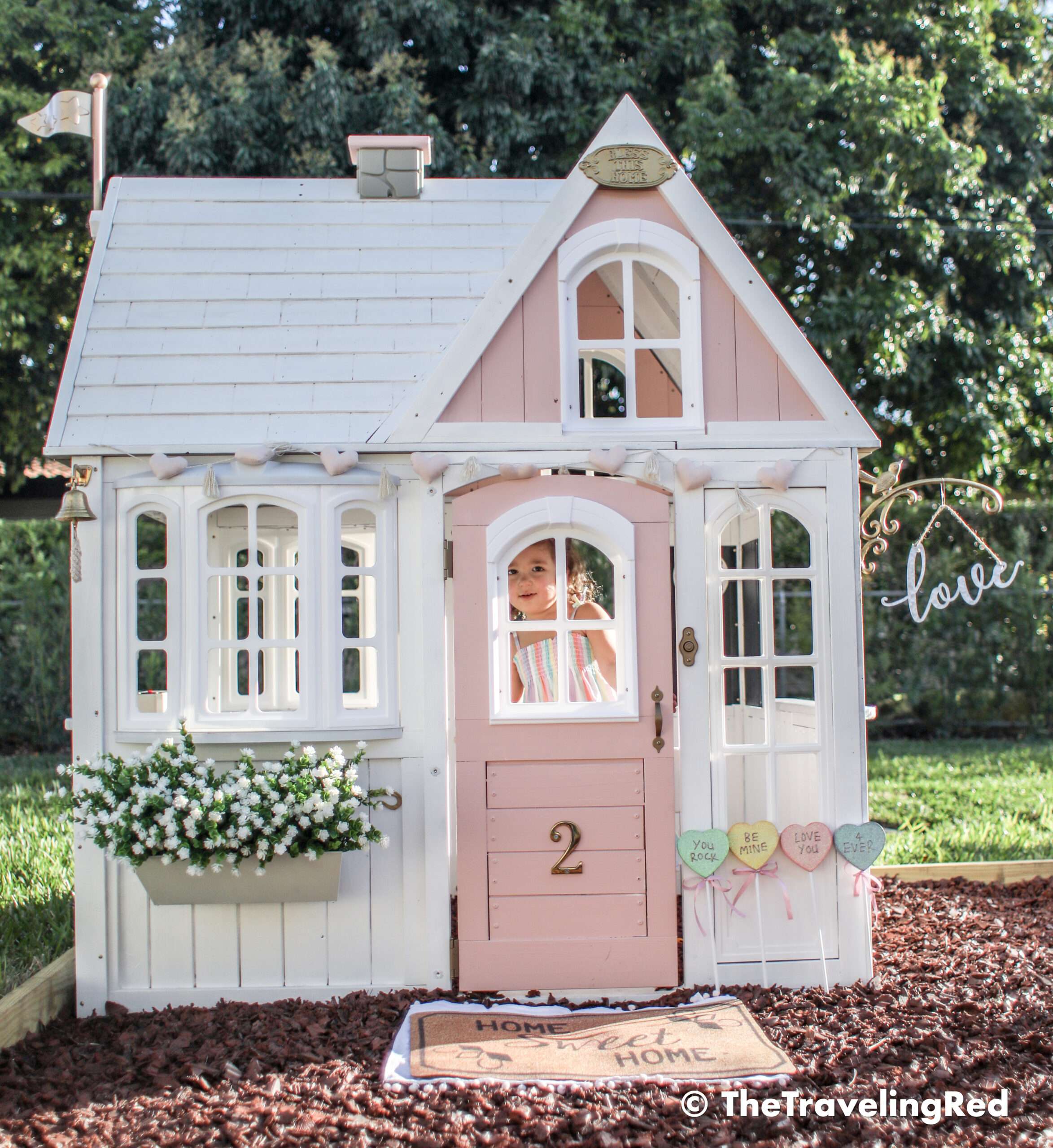 Valentine's Day Playhouse Decor - Kid's outdoor playhouse makeover decorated for Valentines Day using garland, candies and a little sign. Pink & white outdoor playhouse #valentinesday #valentinesdaydecor #homedecor #playhouse #playhousemakeover #valentinesdayhomedecor
