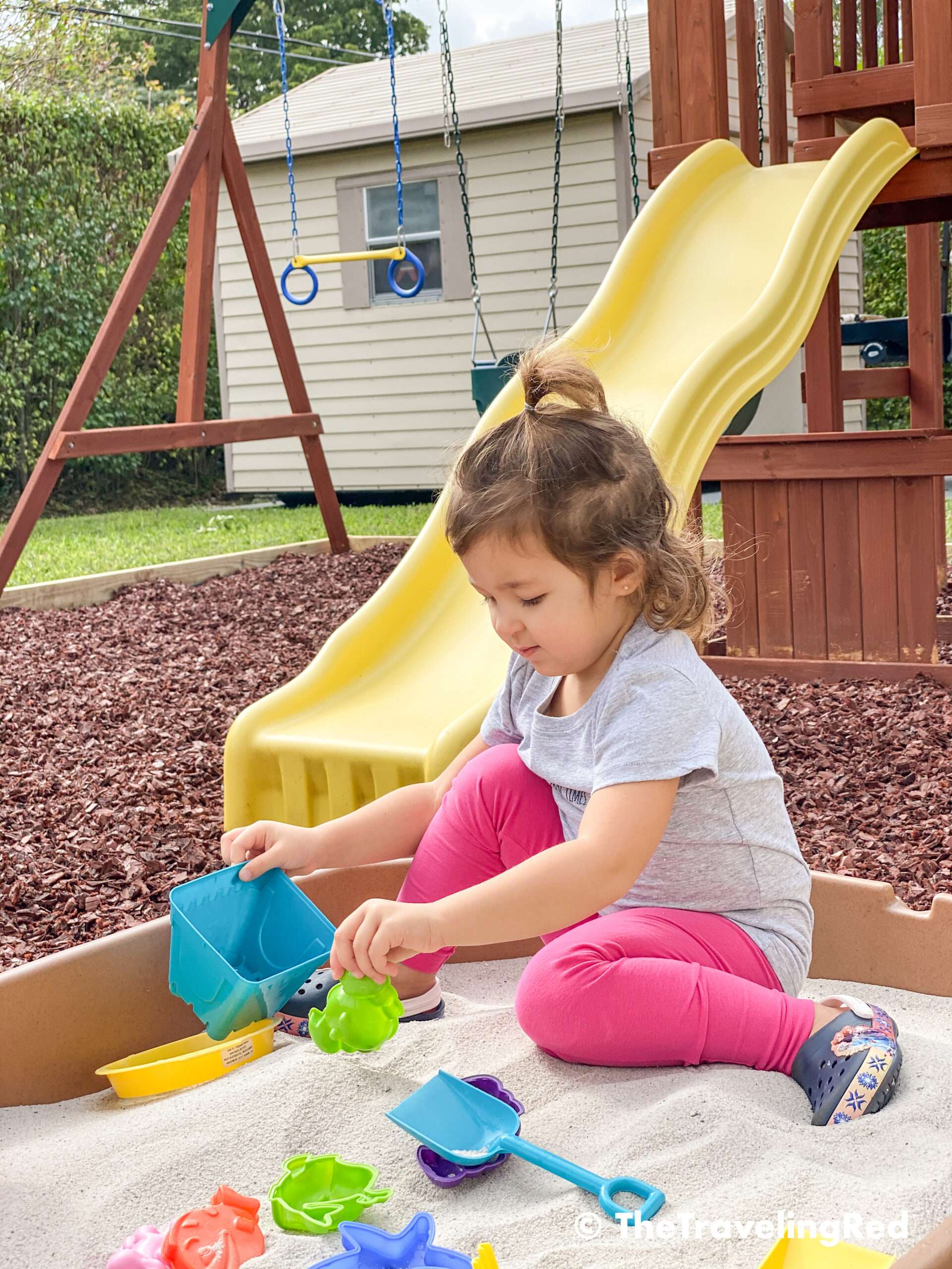 How we built a custom backyard playground with rubber mulch for our swingset, playhouse and sand box. Our sandbox is filled with beach toys and she loves playing in it. This outdoor playground is perfect little outdoor play space for your kids and it's soft on the feet.