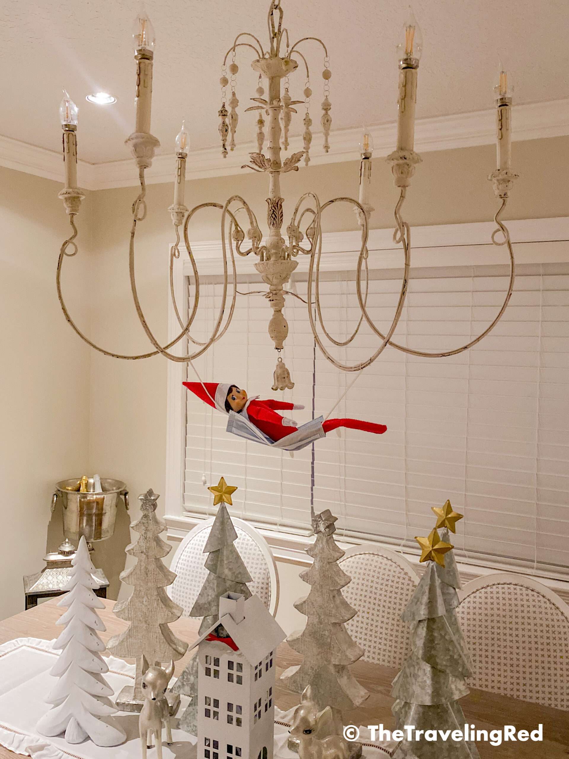 Naughty Elf on the shelf uses a disposable face mask as a hammock and put it on our chandelier. Fun and easy elf on the shelf ideas for a naughty elf that are quick and easy using things you have at home.