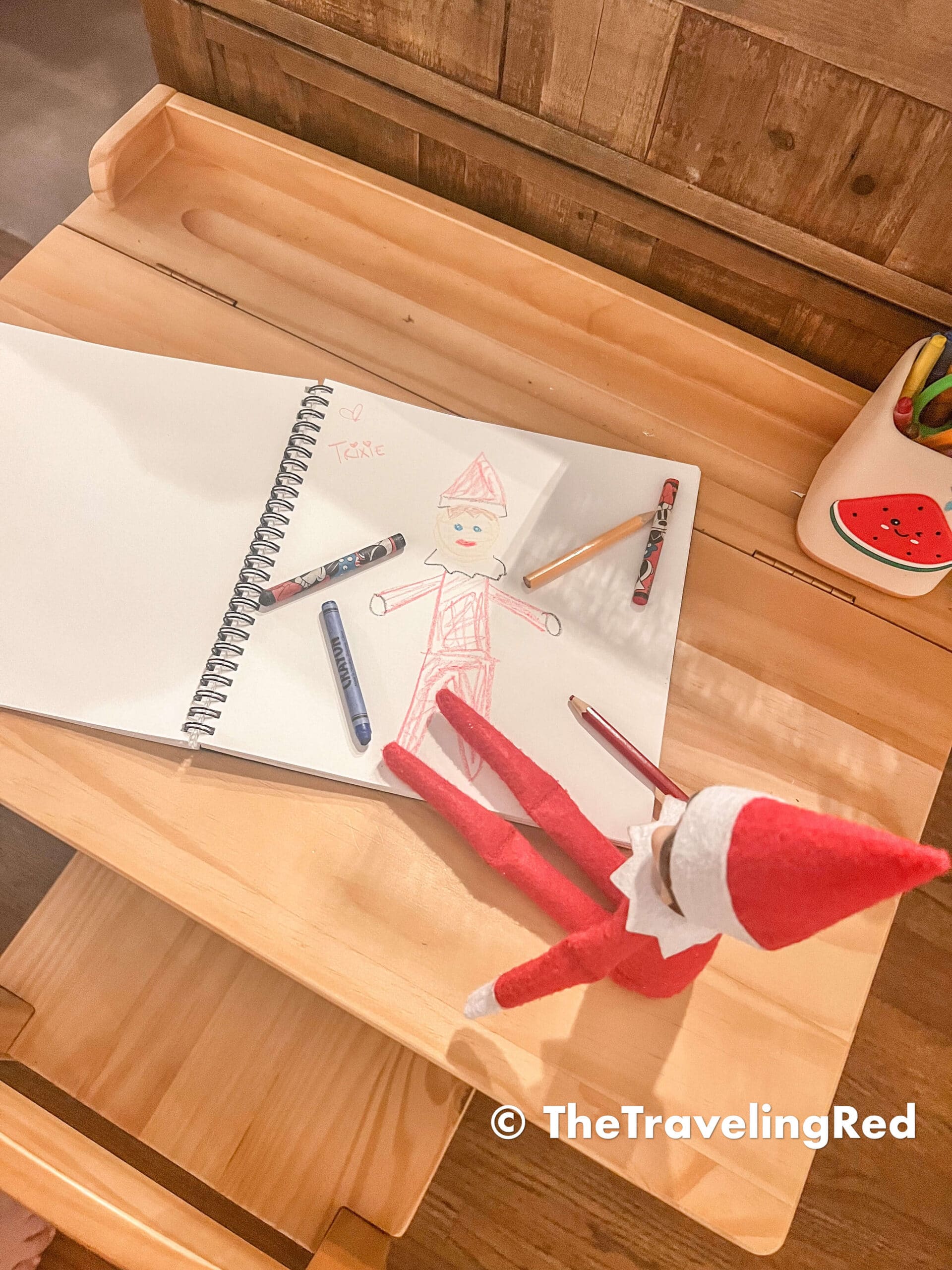 Naughty Elf on the shelf drew an Elf Portrait. Kinda like a self portrait but of an elf. She borrowed the sketch pad and crayons. Fun and easy elf on the shelf ideas for a naughty elf that are quick and easy using things you have at home.
