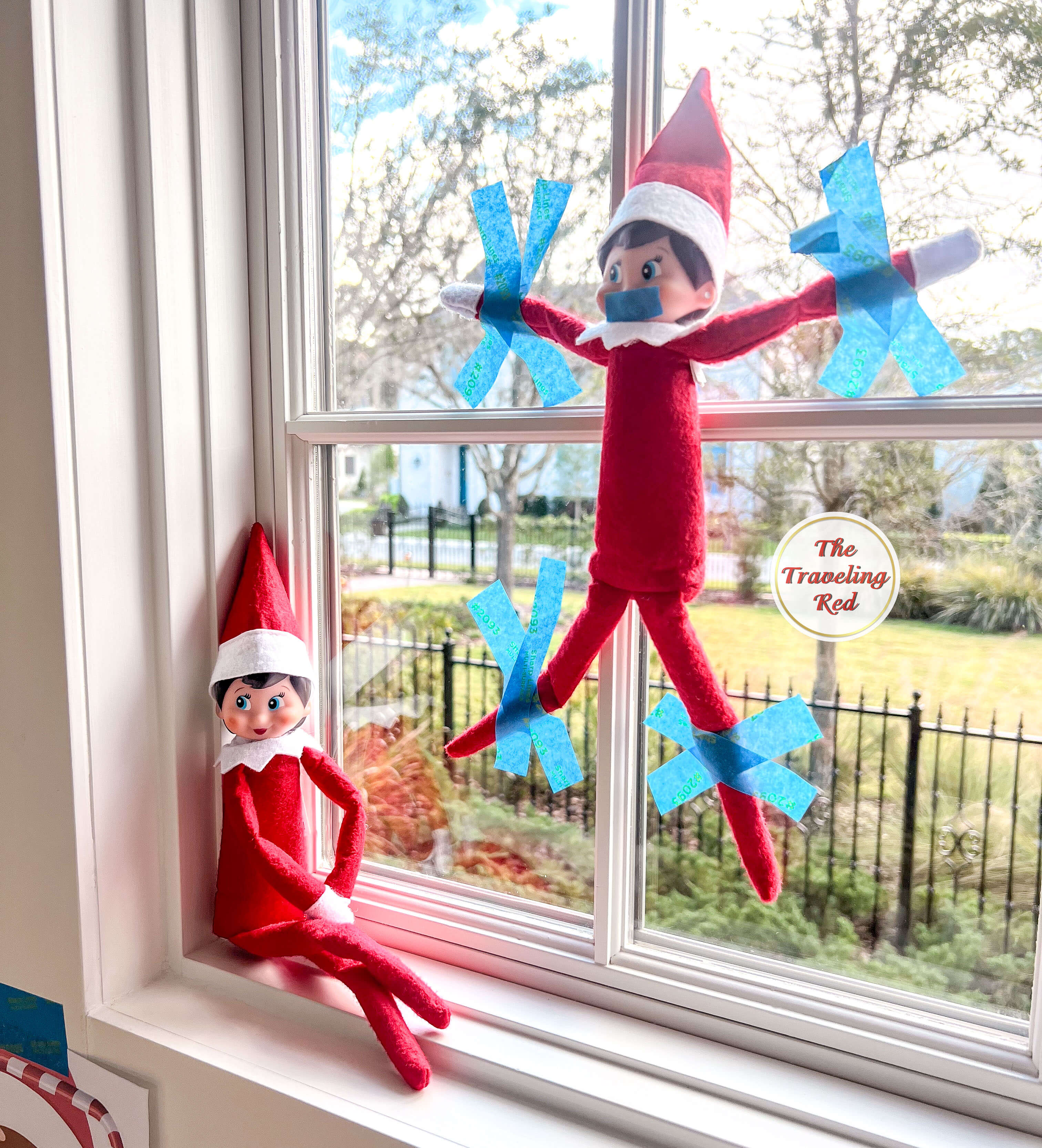 Elf on the Shelf Ideas: Elf found an intruder and taped up the second elf to the window using painters tape. Over 100 easy and quick elf on the shelf ideas that are fun. By The Traveling Red