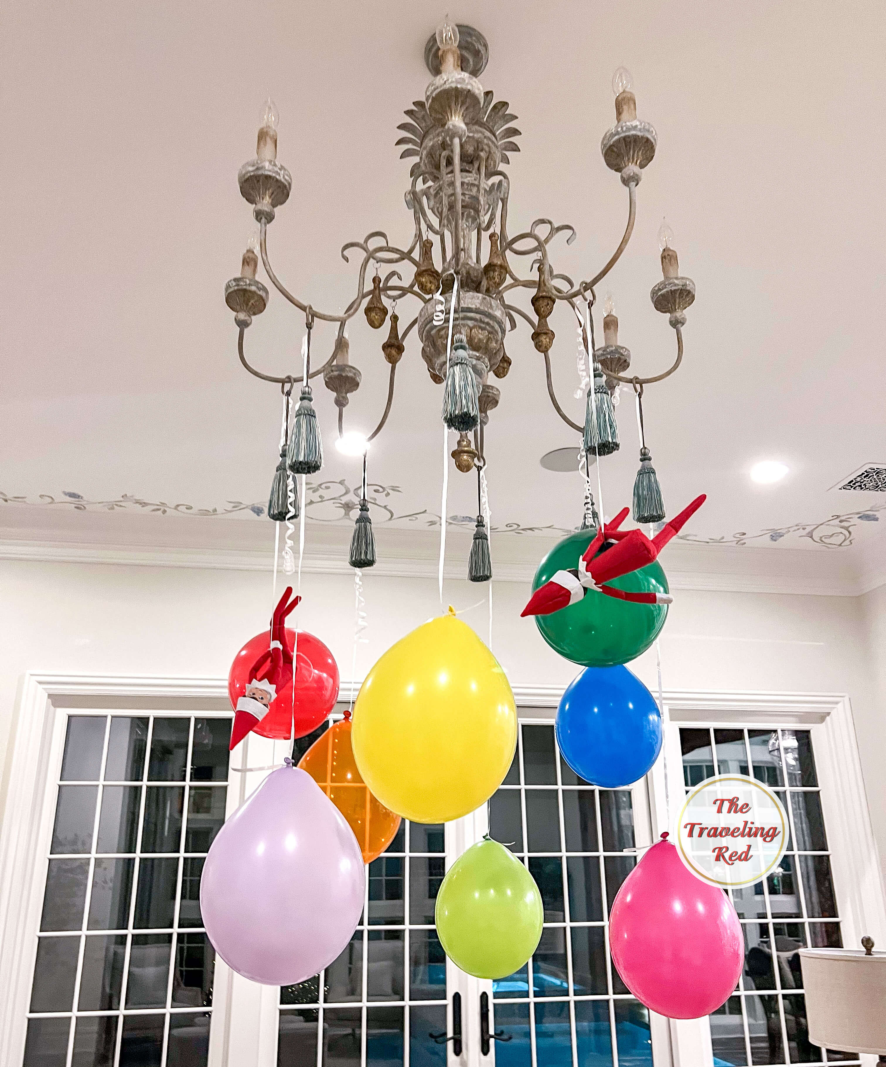 Elf on the Shelf Ideas: Elf hung balloons from the chandelier and both elves are riding balloons like a carnival ride. Over 100 easy and quick elf on the shelf ideas that are fun. By The Traveling Red