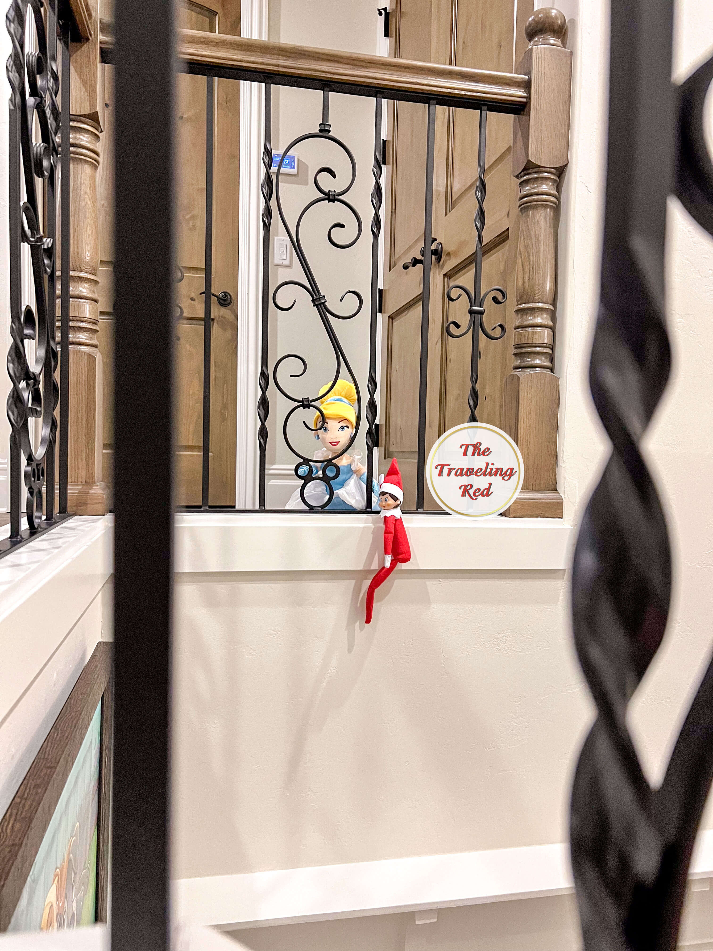 Elf on the Shelf Ideas: Elf is holding onto another dolls hand while suspended in the staircase. Over 100 easy and quick elf on the shelf ideas that are fun. By The Traveling Red