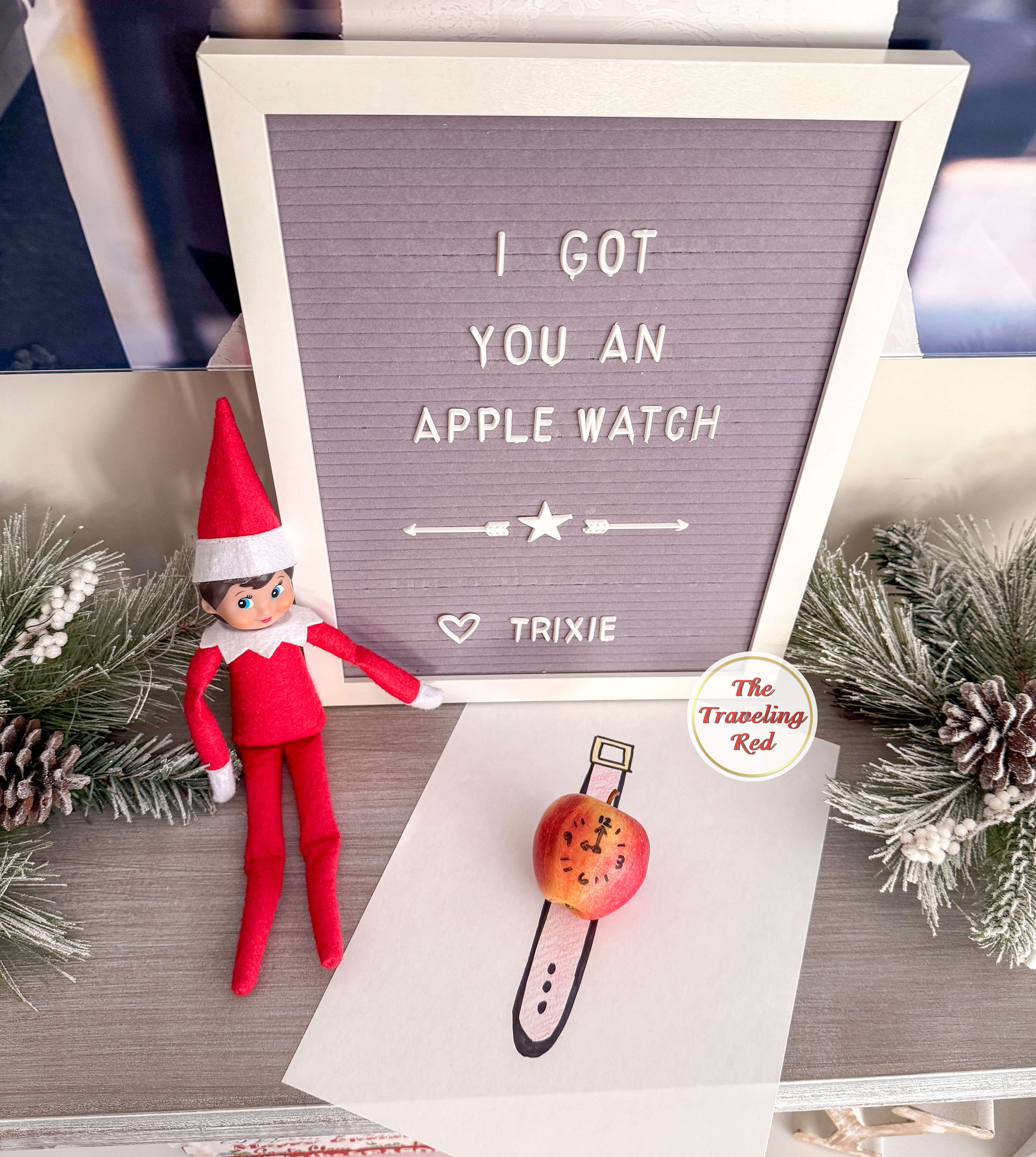 Elf on the Shelf Ideas: Elf made an apple watch by drawing a clock onto an apple using a sharpie and then drawing a watch band on a sheet of paper and putting the apple on top of it. The sign reads I got you an apple watch. Over 100 easy and quick elf on the shelf ideas that are fun. By The Traveling Red
