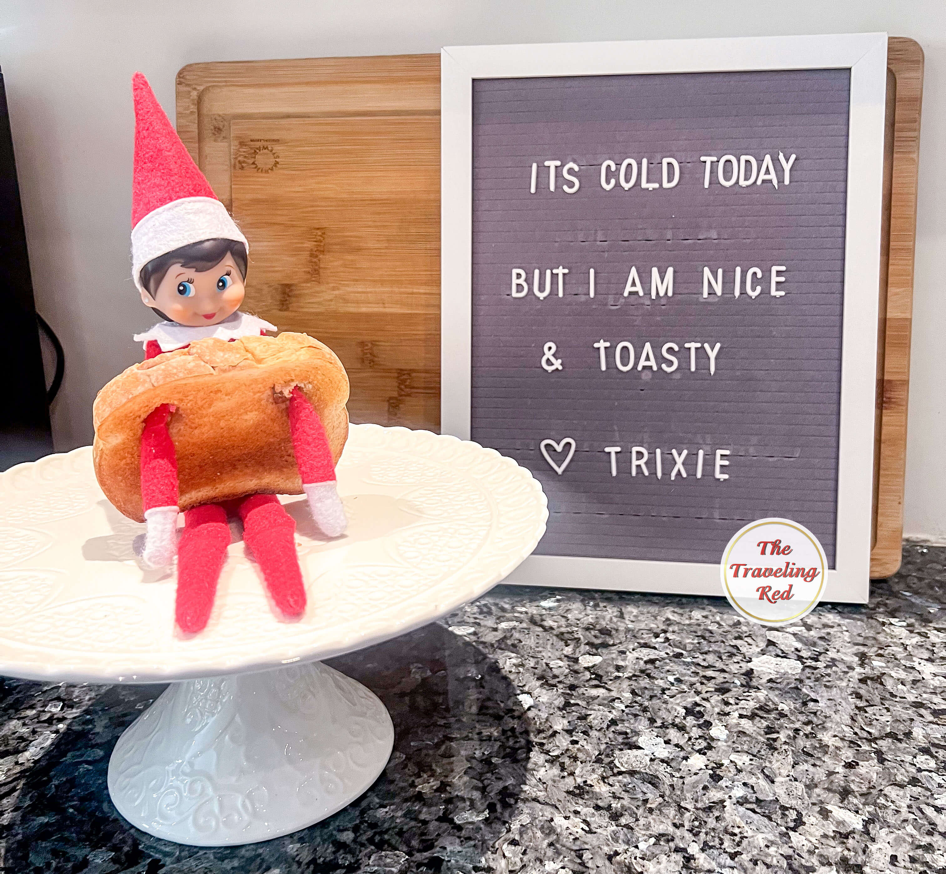 Elf on the Shelf Ideas: Elf is wearing a slice of toasted bread by sticking her arms in it. The message board reads, It's cold today but I am nice and toasty. Over 100 easy and quick elf on the shelf ideas that are fun. By The Traveling Red