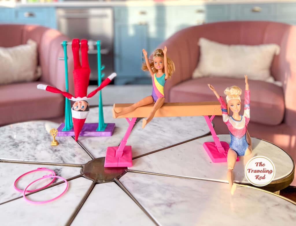 Elf on the Shelf Ideas: Elf is with the gymnastics barbie dolls doing gymnastics on the bars and balance beam. Over 100 easy and quick elf on the shelf ideas that are fun. By The Traveling Red