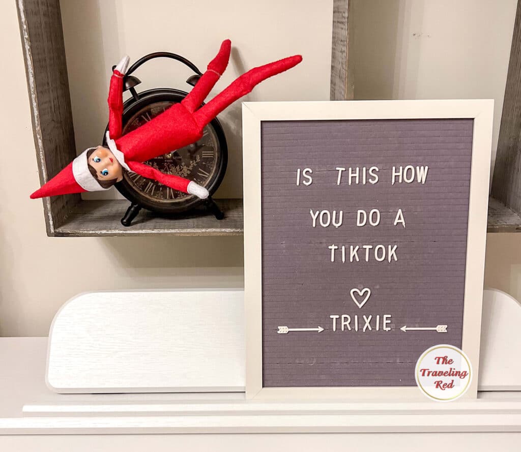 Elf on the Shelf Ideas: Elf is on a clock and the message board reads is this how you do a TikTok. Over 100 easy and quick elf on the shelf ideas that are fun. By The Traveling Red