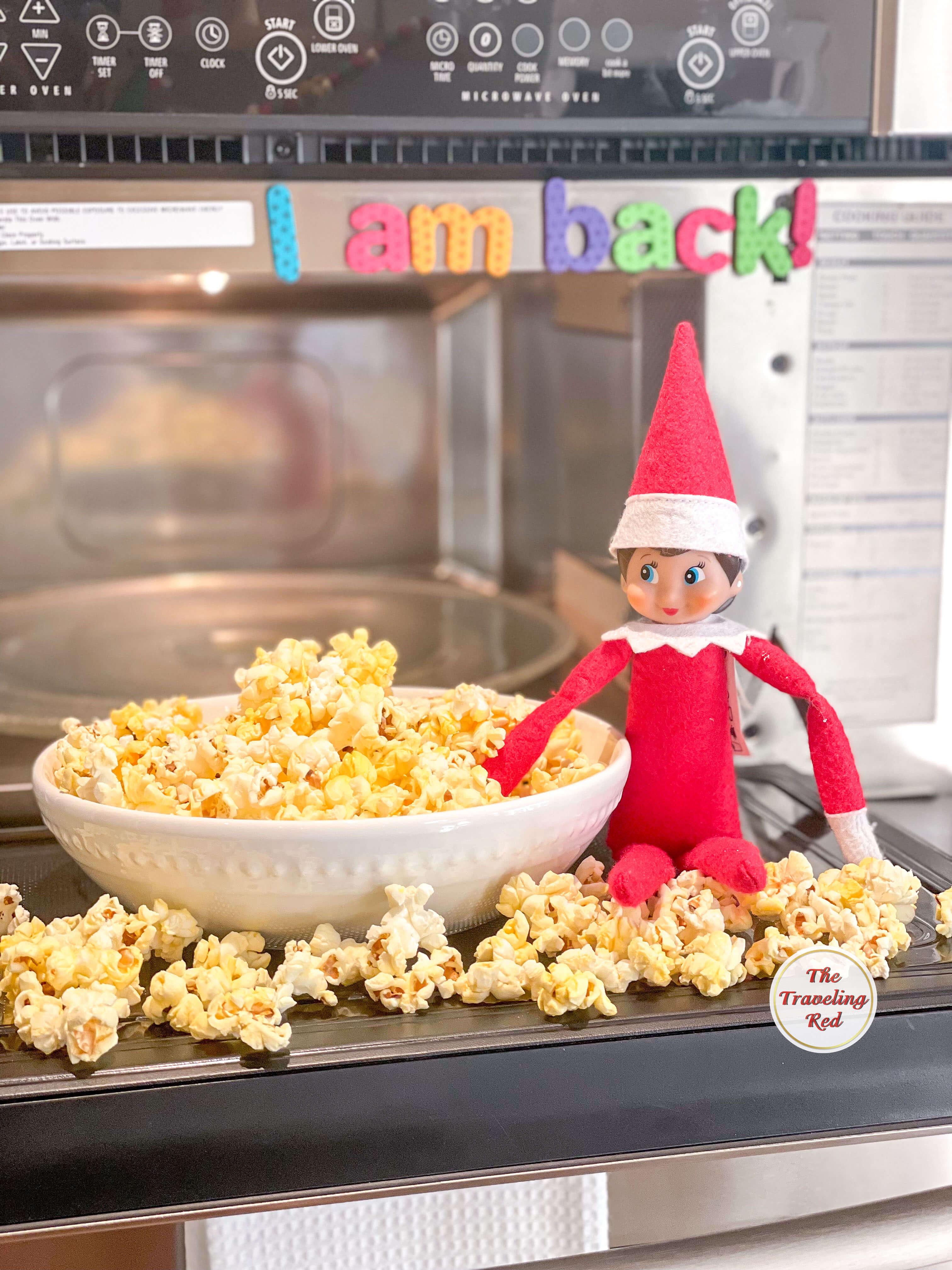 Elf on the Shelf Ideas: Elf made popcorn and is sitting on the open microwave with popcorn falling out all over the microwave and onto the floor. Over 100 easy and quick elf on the shelf ideas that are fun. By The Traveling Red