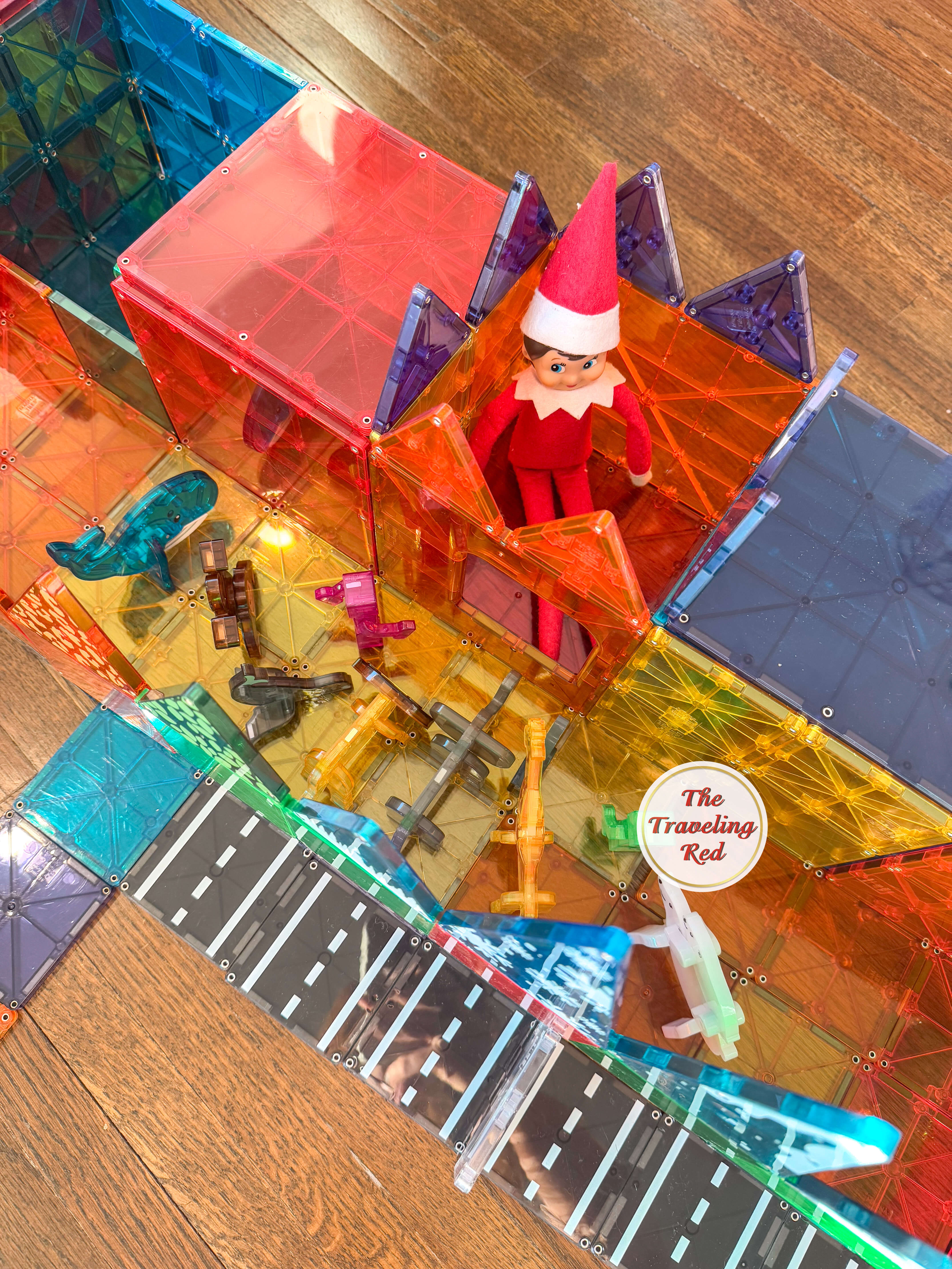 Elf on the Shelf Ideas: Elf is inside a structure built from Magnatiles and outside there people and animals watching him like a zoo. Over 100 easy and quick elf on the shelf ideas that are fun. By The Traveling Red