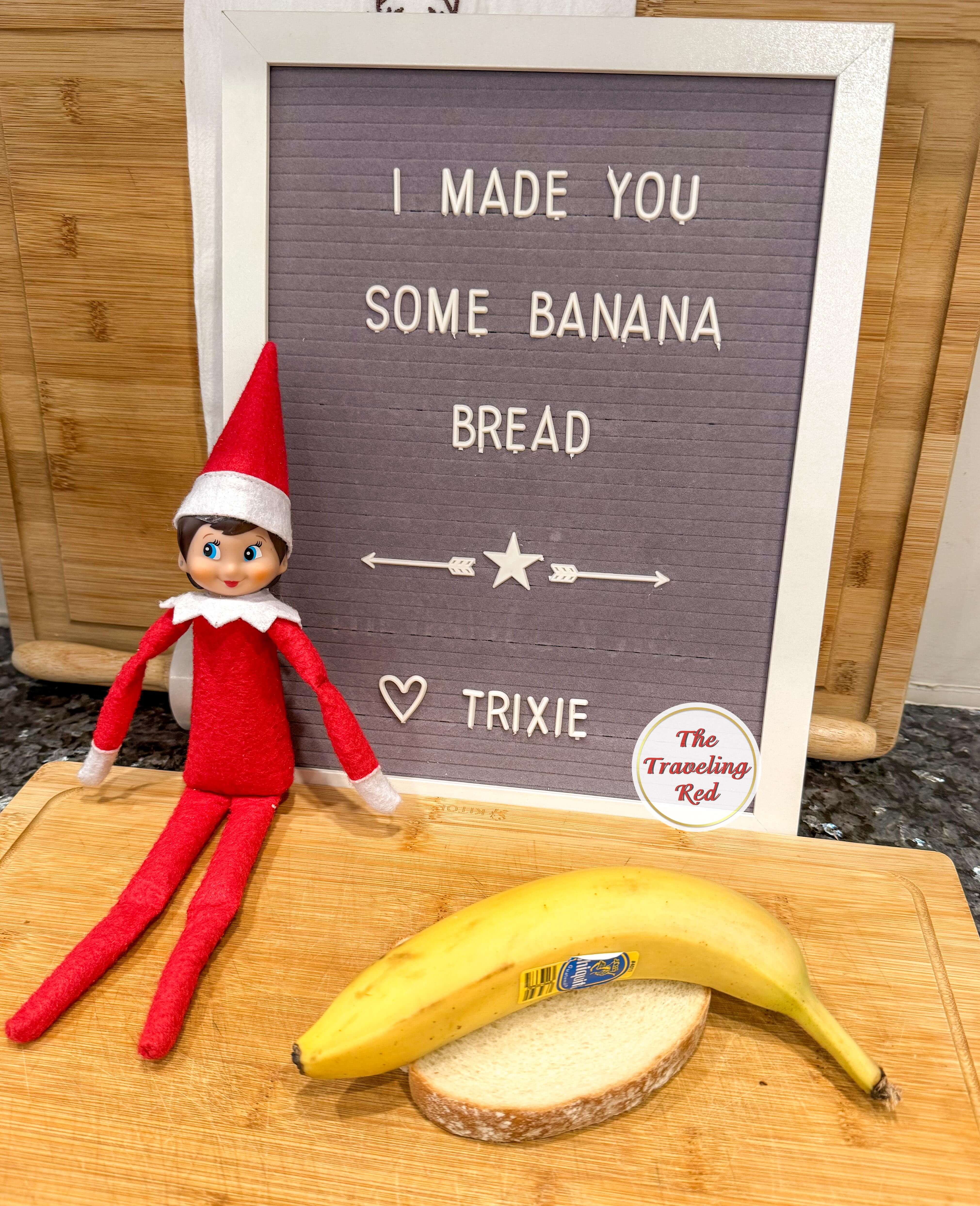 Elf on the Shelf Ideas: Elf is sitting next to a message board that says I made banana bread. Next to that there is a slice of bread with a banana on top of it. Over 100 easy and quick elf on the shelf ideas that are fun. By The Traveling Red