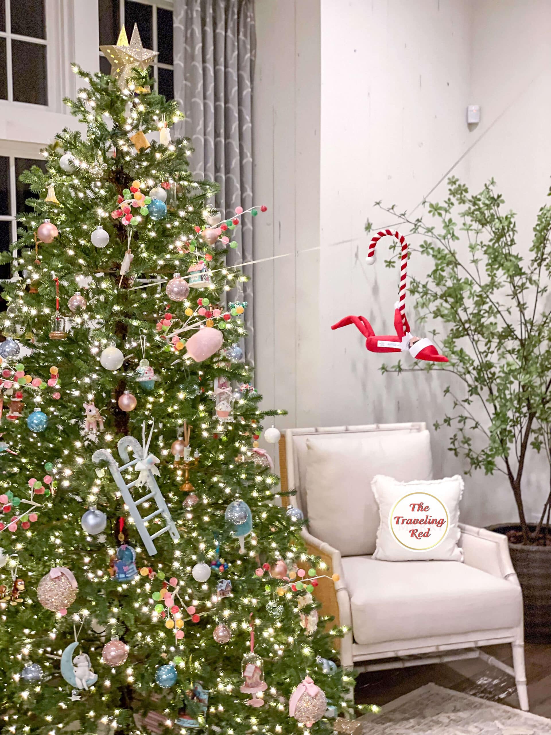 Elf on the Shelf Ideas: Elf is hanging from a zip line she created using a ribbon she attached from the chandelier to the christmas tree and is hanging from a candy cane. Over 100 easy and quick elf on the shelf ideas that are fun. By The Traveling Red