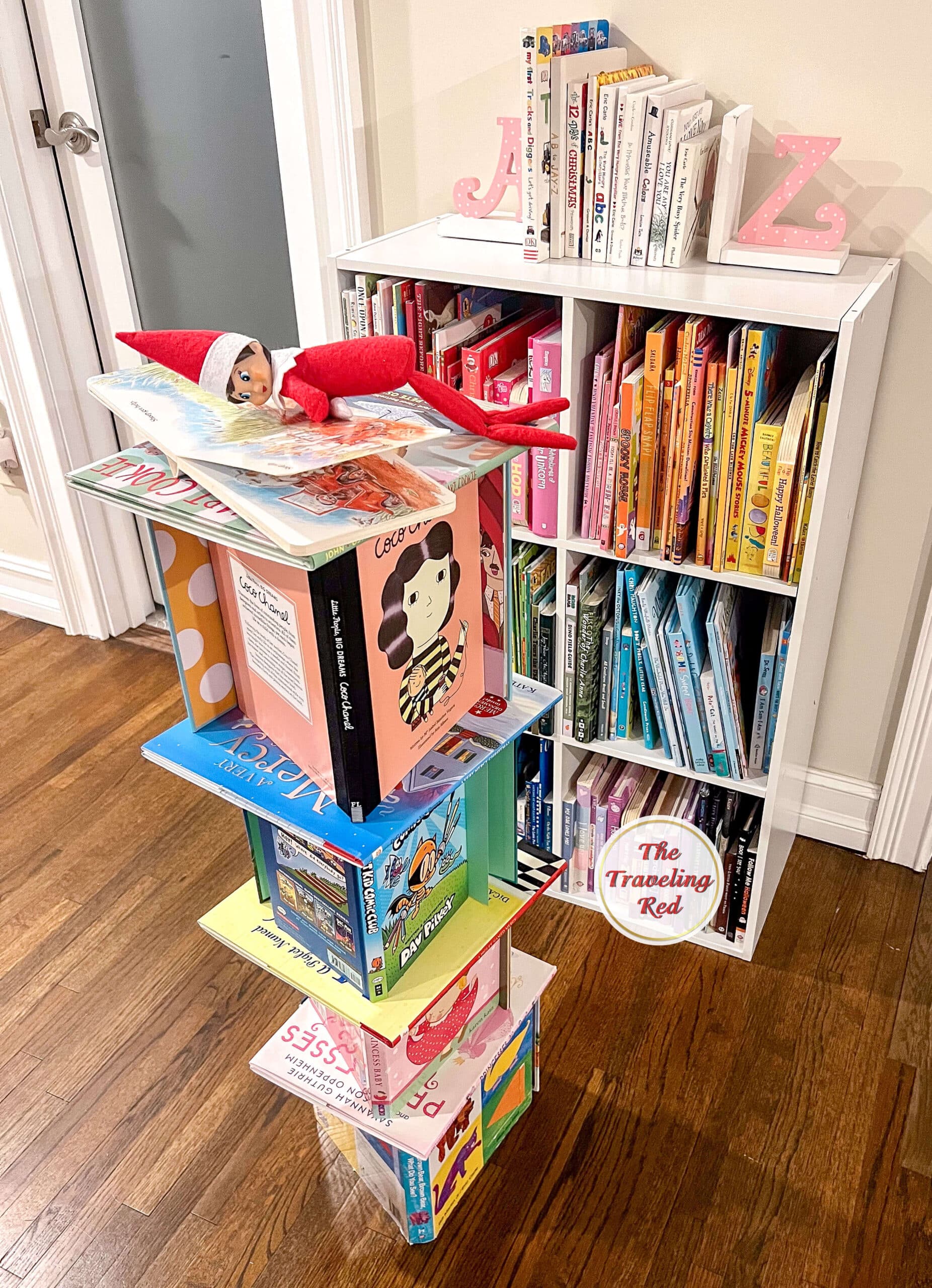 Elf on the Shelf Ideas: Elf made a tower out of books and is on the top reading a book. Over 100 easy and quick elf on the shelf ideas that are fun. By The Traveling Red