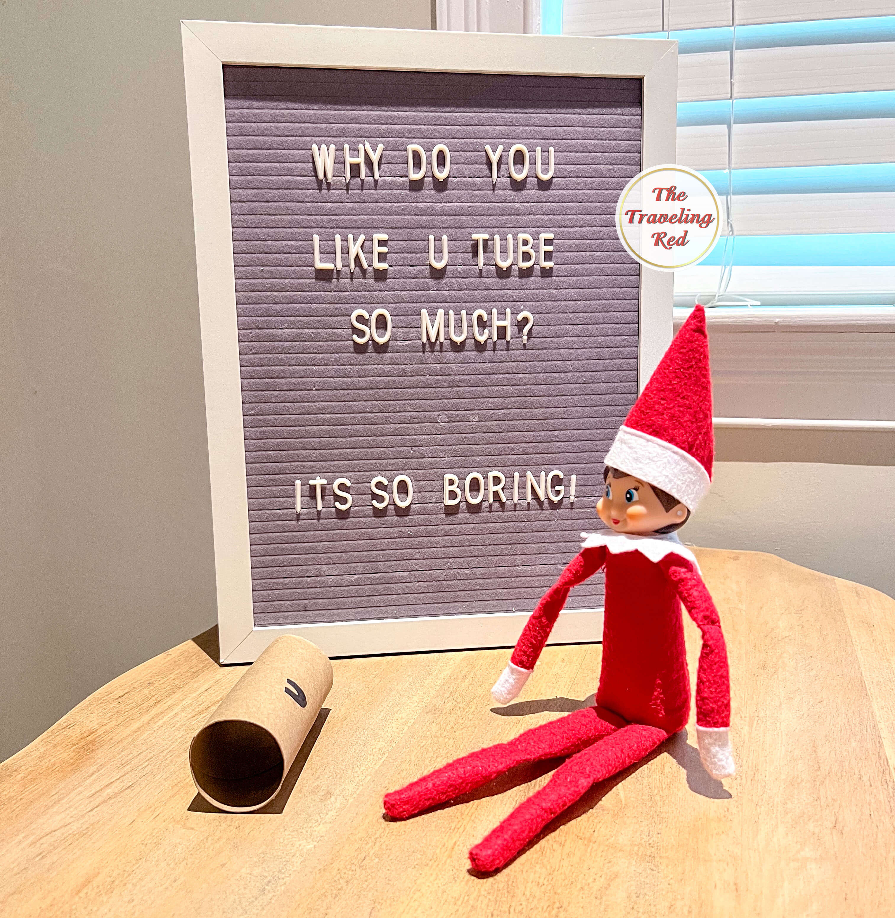 Elf on the Shelf Ideas: Elf is sitting on a table with an empty toilet paper roll in front of it and the tube has a U painted on it. The message board behind it reads " Why do you like U Tube so much?" It's a play on the word YouTube. Over 100 easy and quick elf on the shelf ideas that are fun. By The Traveling Red