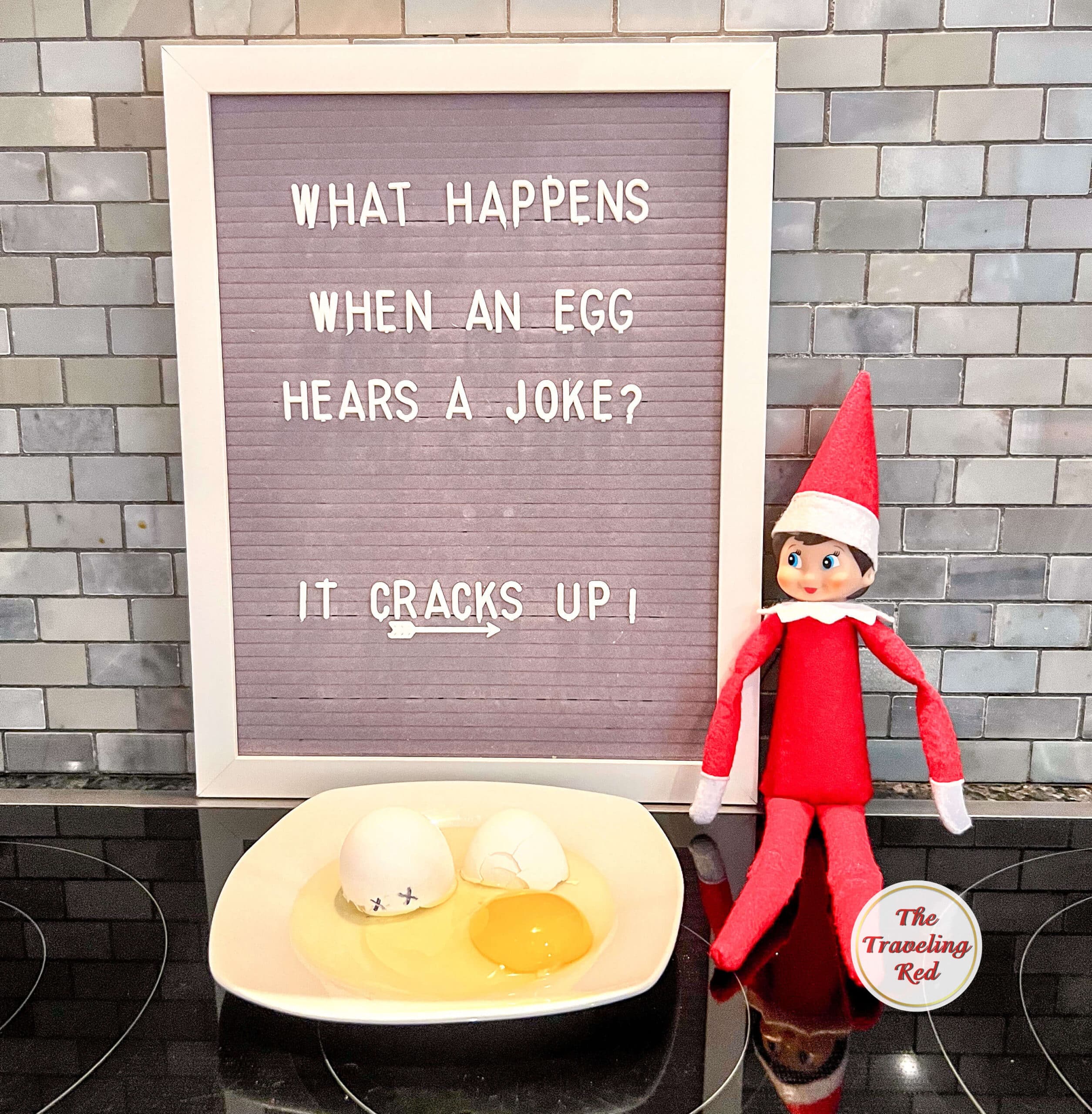 Elf on the Shelf Ideas: Elf is next to a plate with a cracked egg. The shell has a face drawn on it. The message board behind it reads "What happens when you tell an egg a joke? It cracks up." Over 100 easy and quick elf on the shelf ideas that are fun. By The Traveling Red