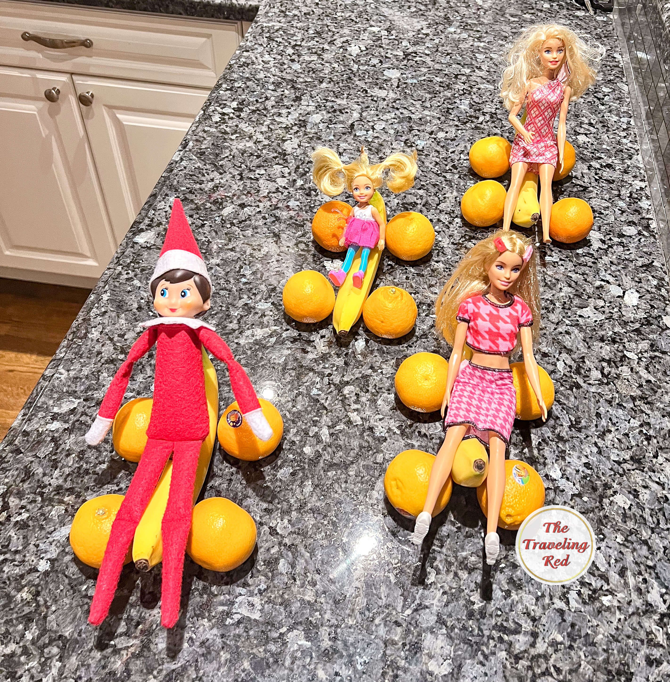 Elf on the Shelf Ideas: Elf got together with some barbies and had a race. They used 4 oranges and 1 banana to create a car. Each of the 4 dolls has their own fruit car and they're racing. Over 100 easy and quick elf on the shelf ideas that are fun. By The Traveling Red