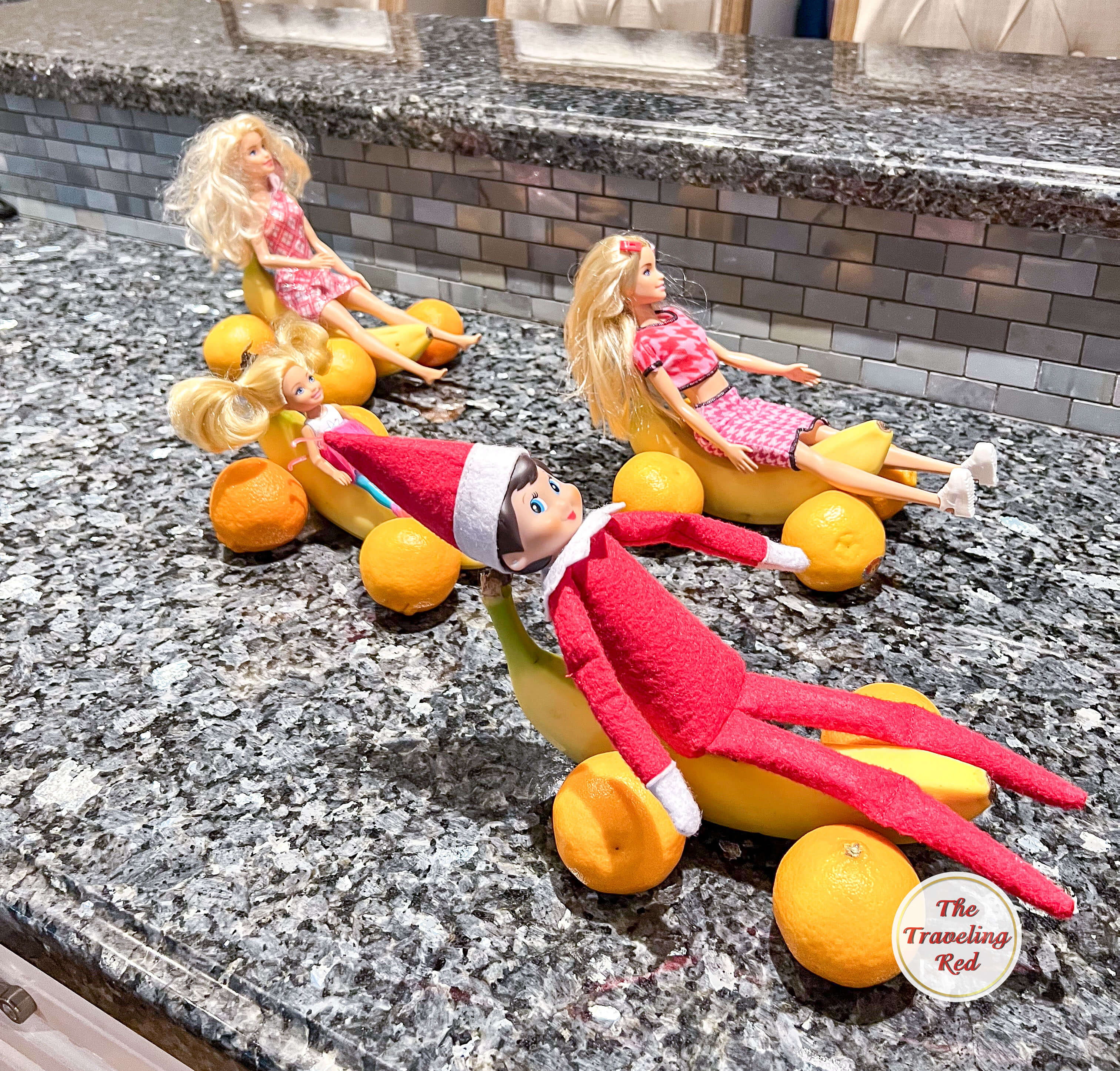 Elf on the Shelf Ideas: Elf got together with some barbies and had a race. They used 4 oranges and 1 banana to create a car. Each of the 4 dolls has their own fruit car and they're racing. Over 100 easy and quick elf on the shelf ideas that are fun. By The Traveling Red