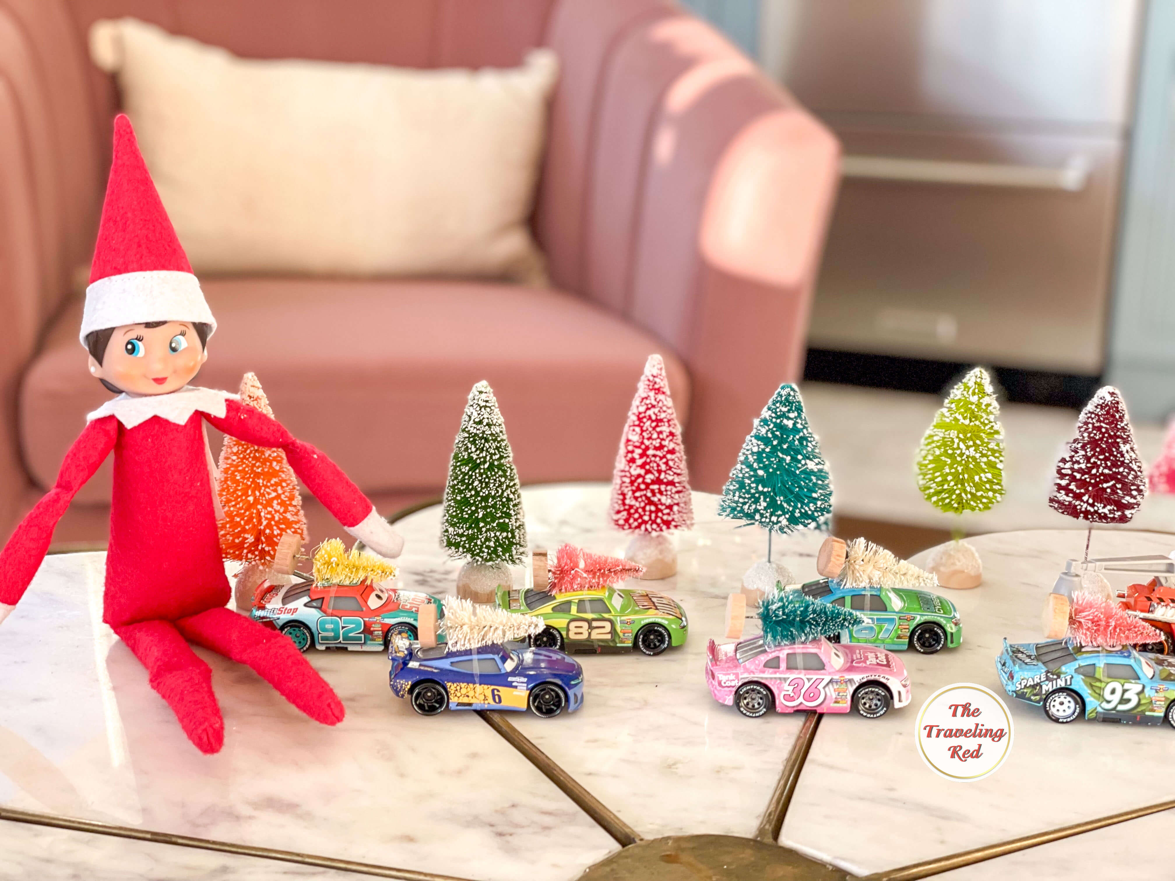 Elf on the Shelf Ideas: Elf is next to little hot wheels cars that have miniature trees on their roofs. Over 100 easy and quick elf on the shelf ideas that are fun. By The Traveling Red