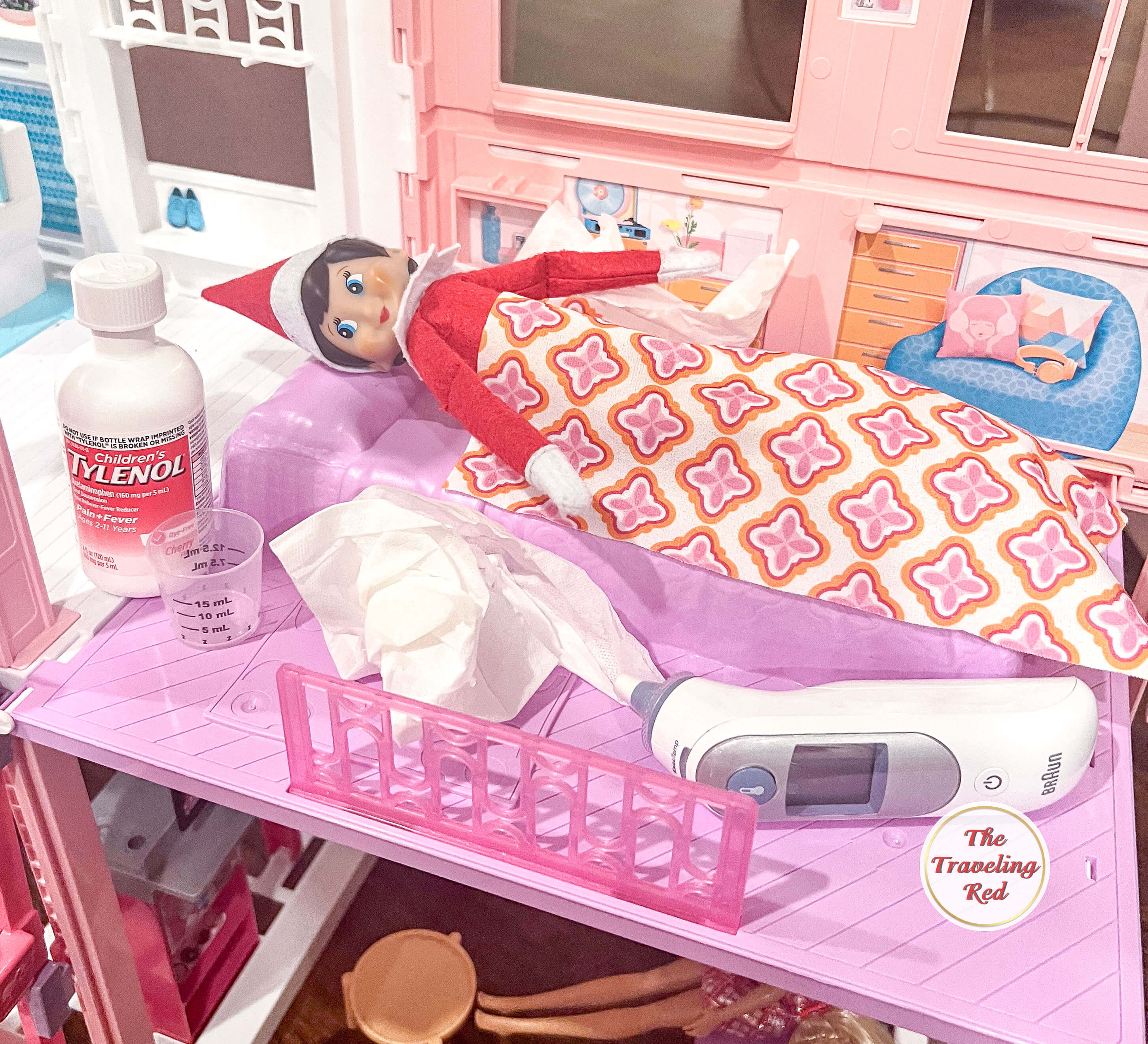 Elf on the Shelf Ideas: Elf is in bed in the barbie house surrounded by medicine, a thermometer and tissues because she is having a sick day. Over 100 easy and quick elf on the shelf ideas that are fun. By The Traveling Red