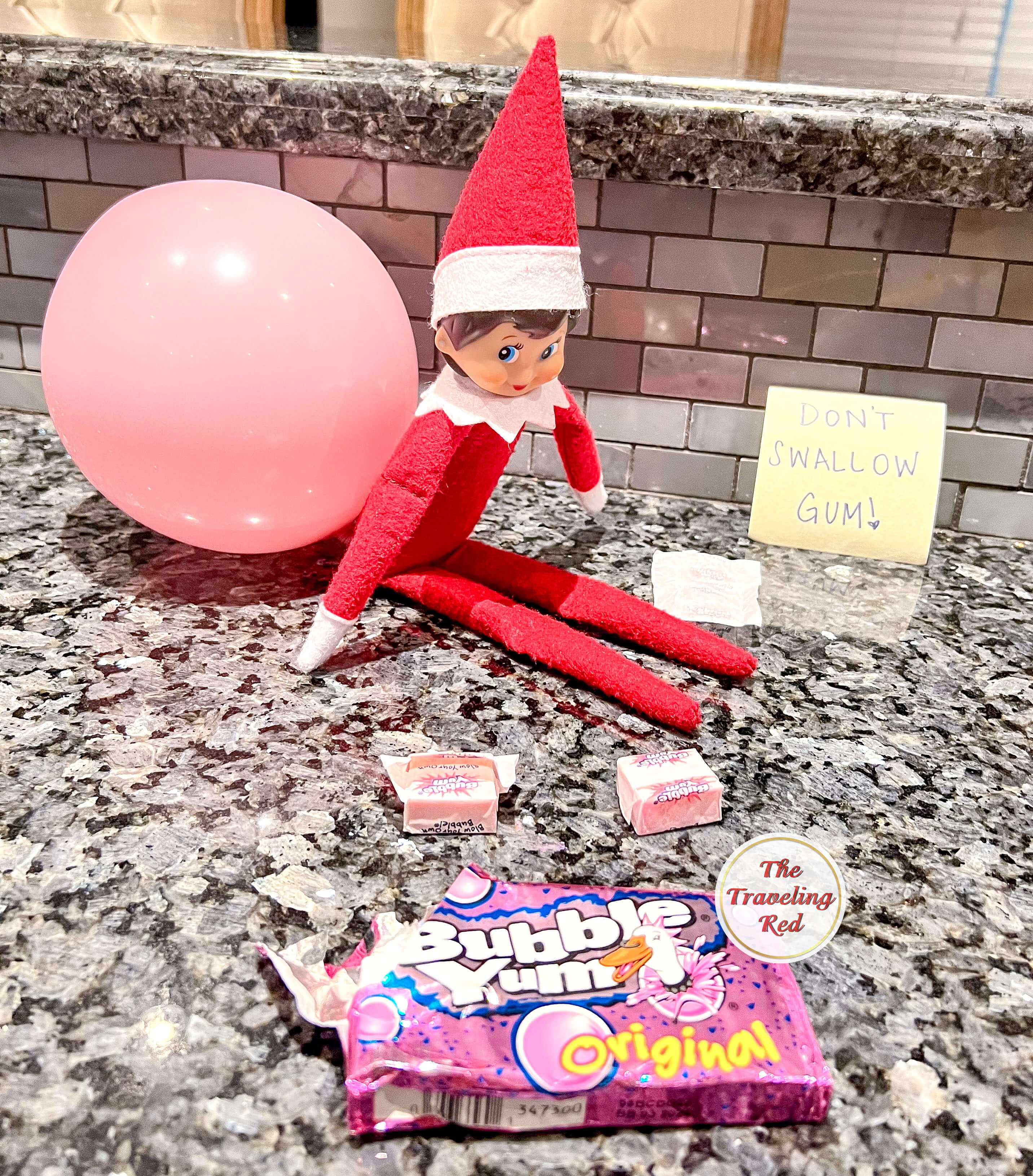Elf on the Shelf Ideas: Elf is sitting on the counter next to bubble gum and there's a pink balloon coming out of the elf's butt. The sign says "Do not swallow bubble gum". Over 100 easy and quick elf on the shelf ideas that are fun. By The Traveling Red