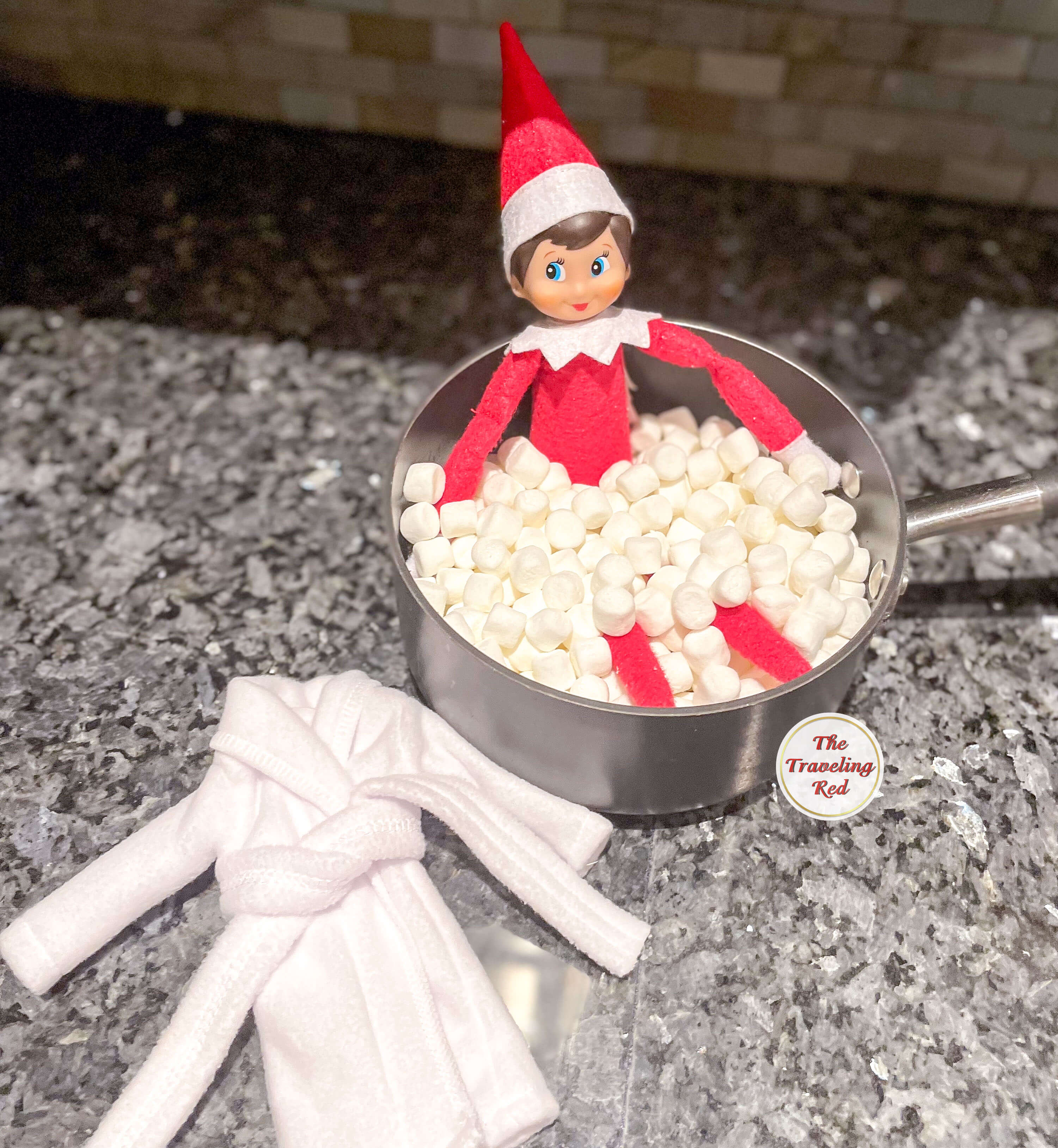 Elf on the Shelf Ideas: Elf is having a spa day. Elf is in a pot that's filled with mini marshmallows and an elf robe next to it. Over 100 easy and quick elf on the shelf ideas that are fun. By The Traveling Red