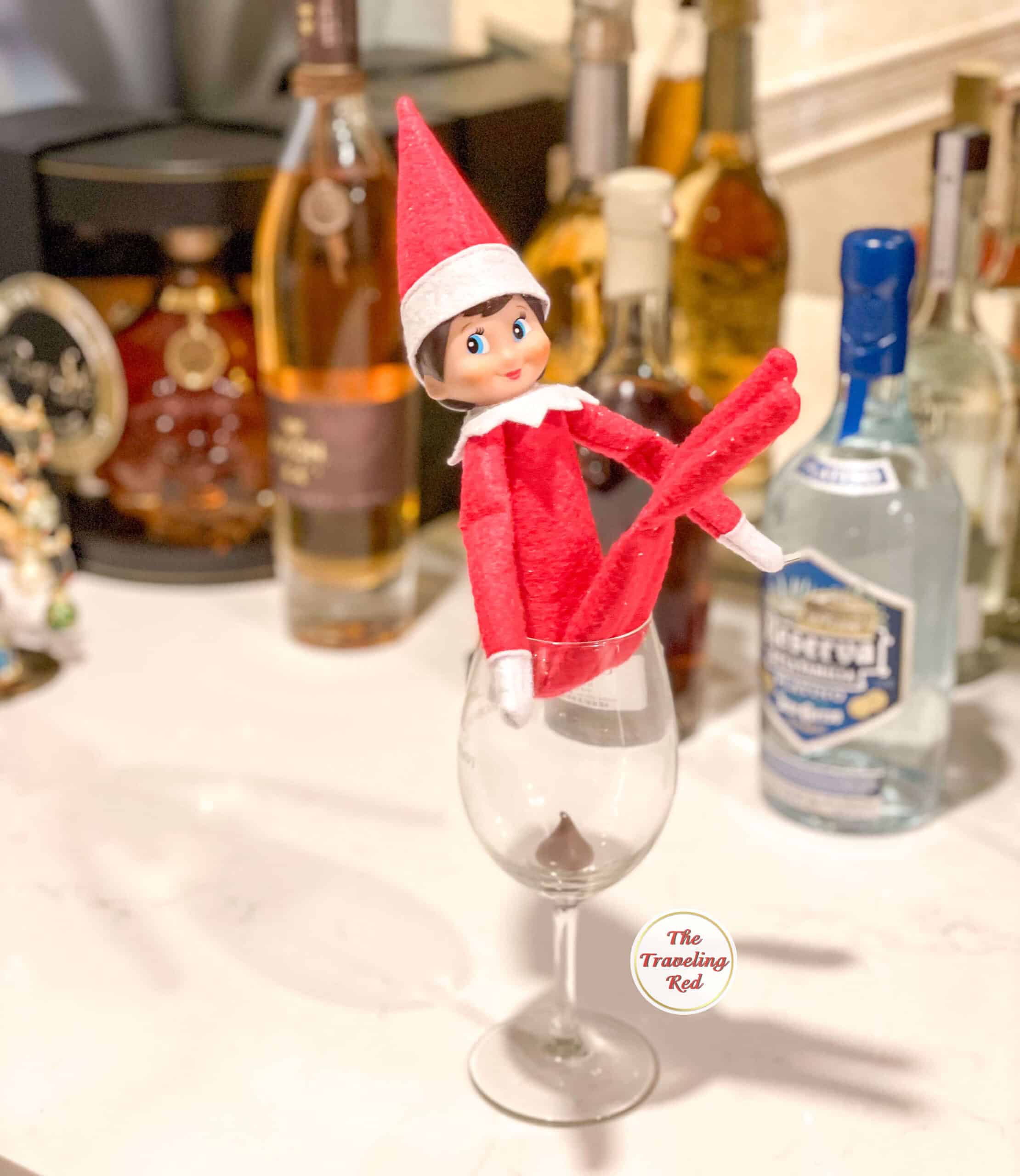 Elf on the Shelf Ideas: Elf is sitting on a wine glass with a hershey kiss in the glass to look like poop. Over 100 easy and quick elf on the shelf ideas that are fun. By The Traveling Red