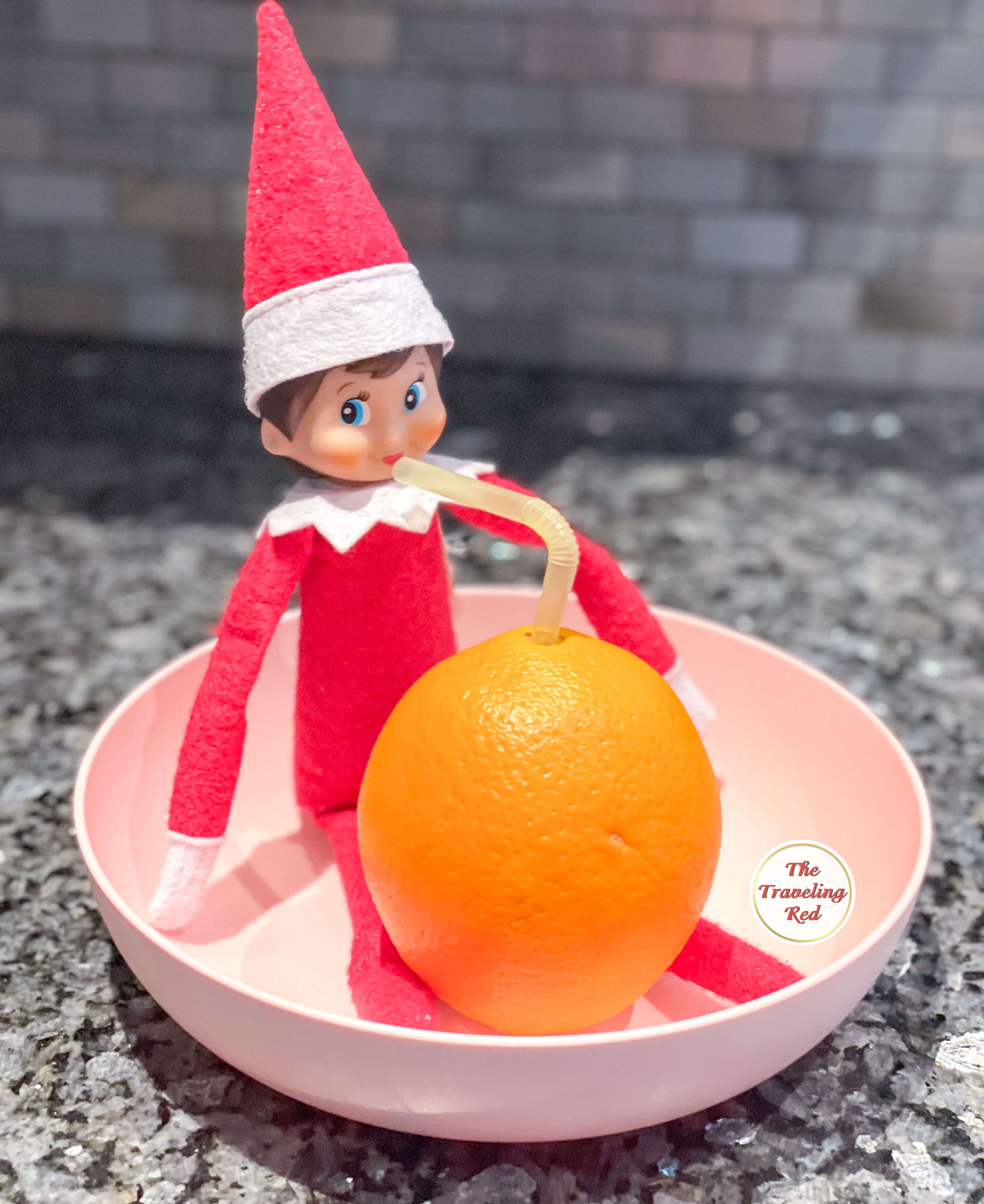 Elf on the Shelf Ideas: Elf is sitting down with an orange and a straw in the orange to look like they're drinking fresh orange juice. Over 100 easy and quick elf on the shelf ideas that are fun. By The Traveling Red
