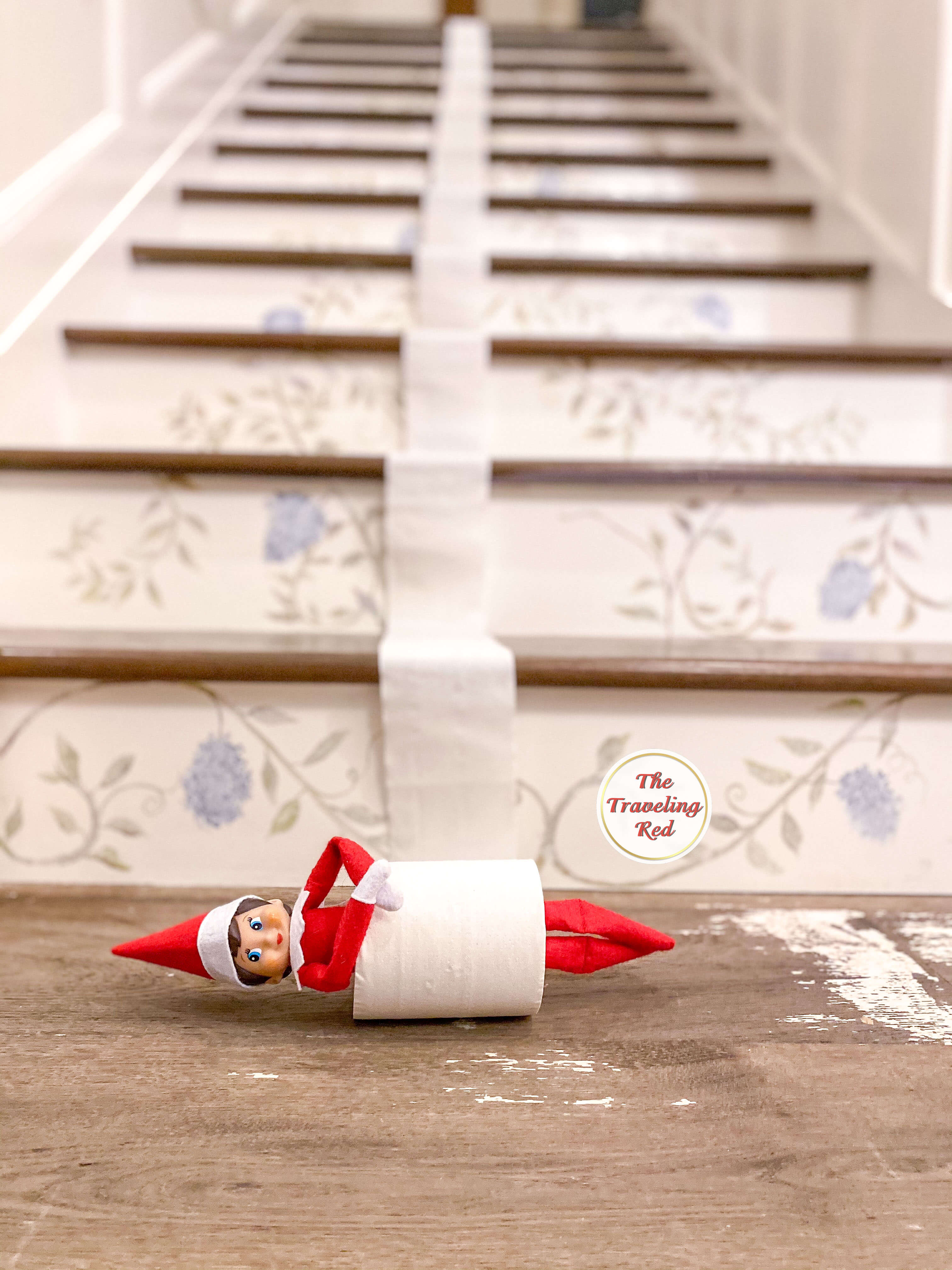 Elf on the Shelf Ideas: Elf is rolling down the stairs inside a roll of toilet paper. The toilet paper is coming down the stairs. Over 100 easy and quick elf on the shelf ideas that are fun. By The Traveling Red