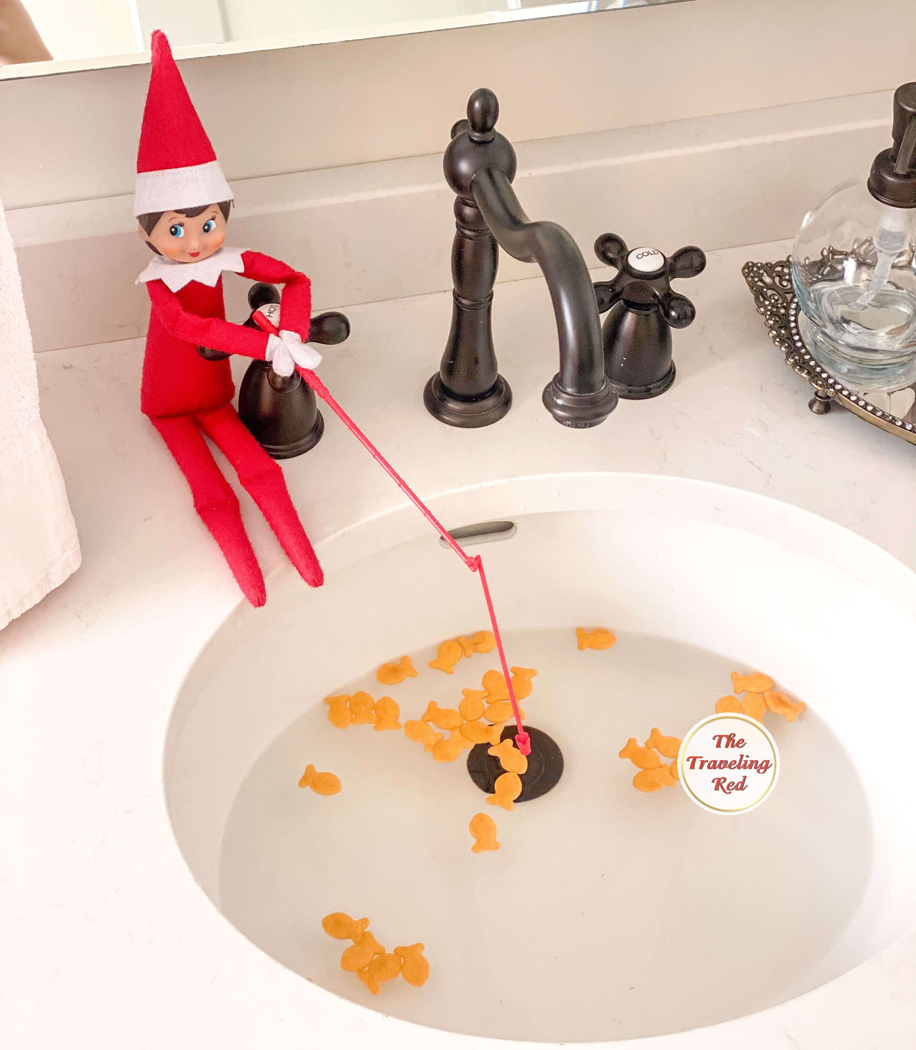 Elf on the Shelf Ideas: Elf is fishing in the sink with goldfish floating. Over 100 easy and quick elf on the shelf ideas that are fun. By The Traveling Red